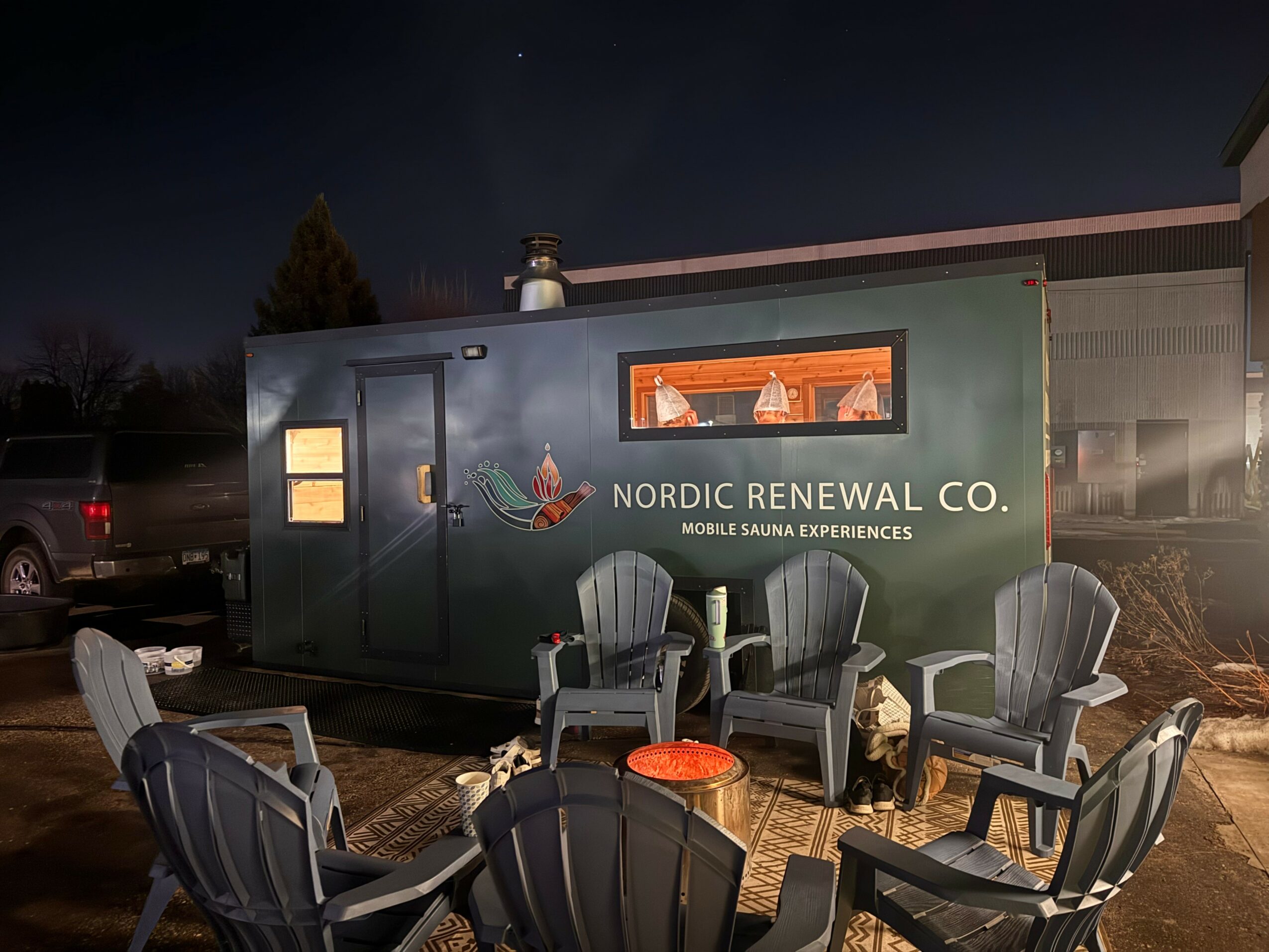 Nighttime scene with a green trailer labeled 'Nordic Renewal Co.' and outdoor chairs in front.