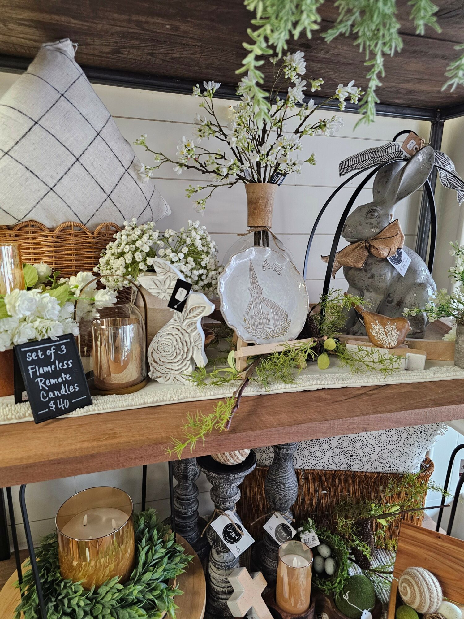 Decorative display with vases, plants, and a pillow on a wooden surface, arranged with flowers and ornaments.