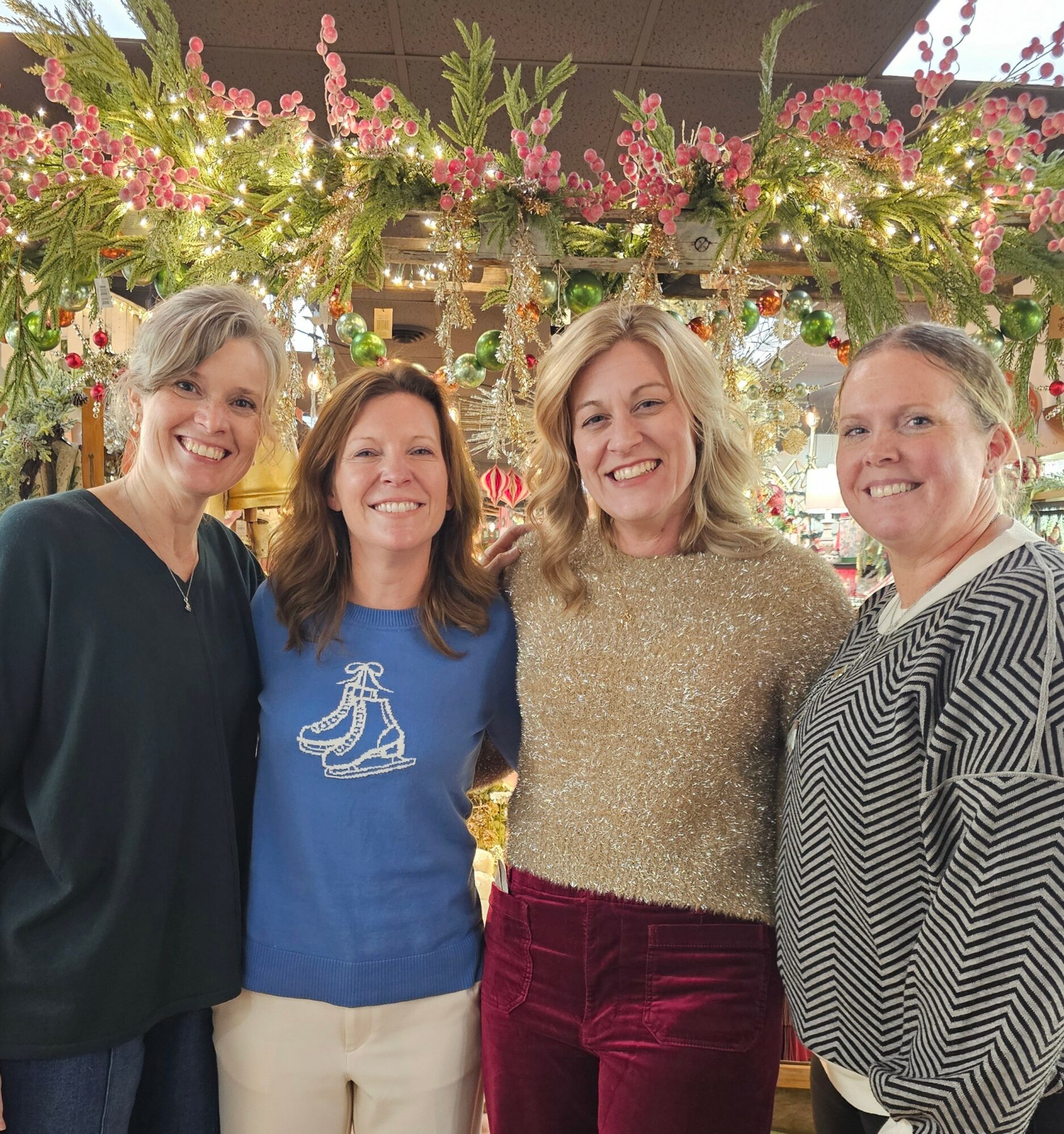 Four women smiling in front of floral decorations, standing close together indoors.