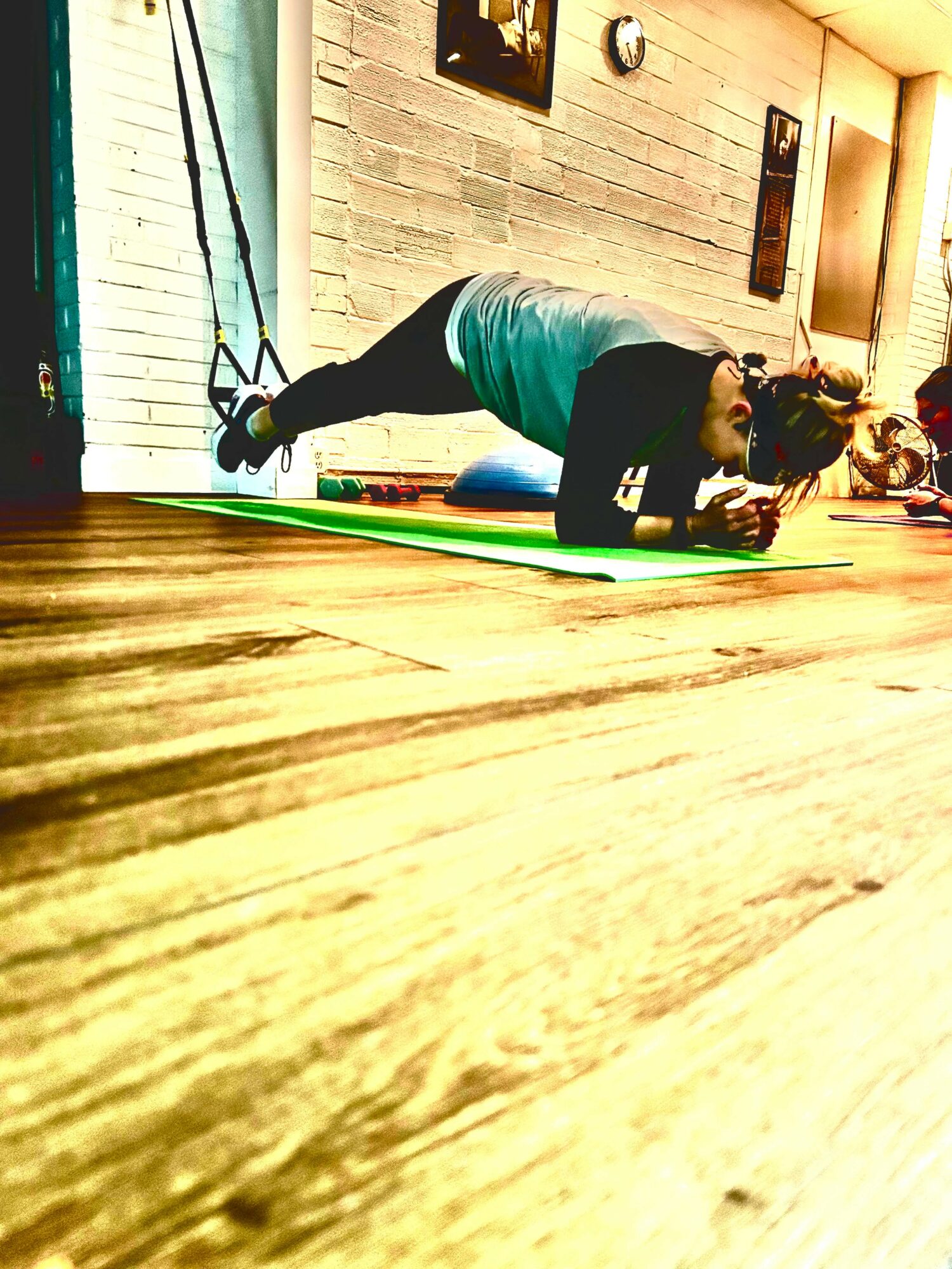 Person doing a plank exercise on a yoga mat in a gym, with resistance bands attached to the wall.