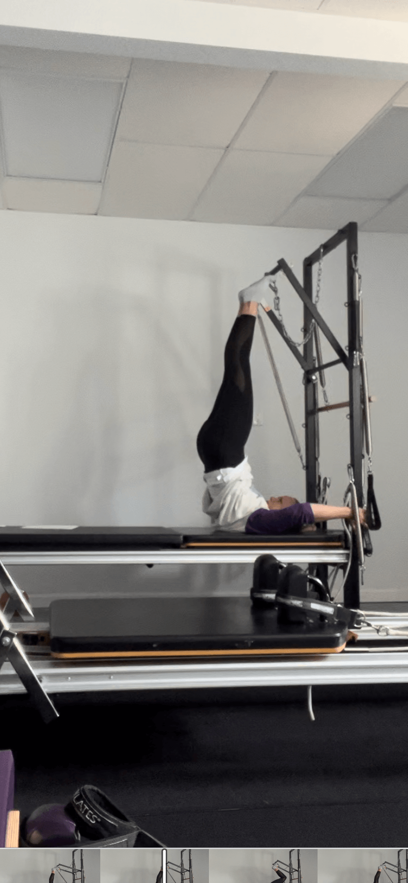 Person performing a headstand on a Pilates reformer machine in a fitness studio.