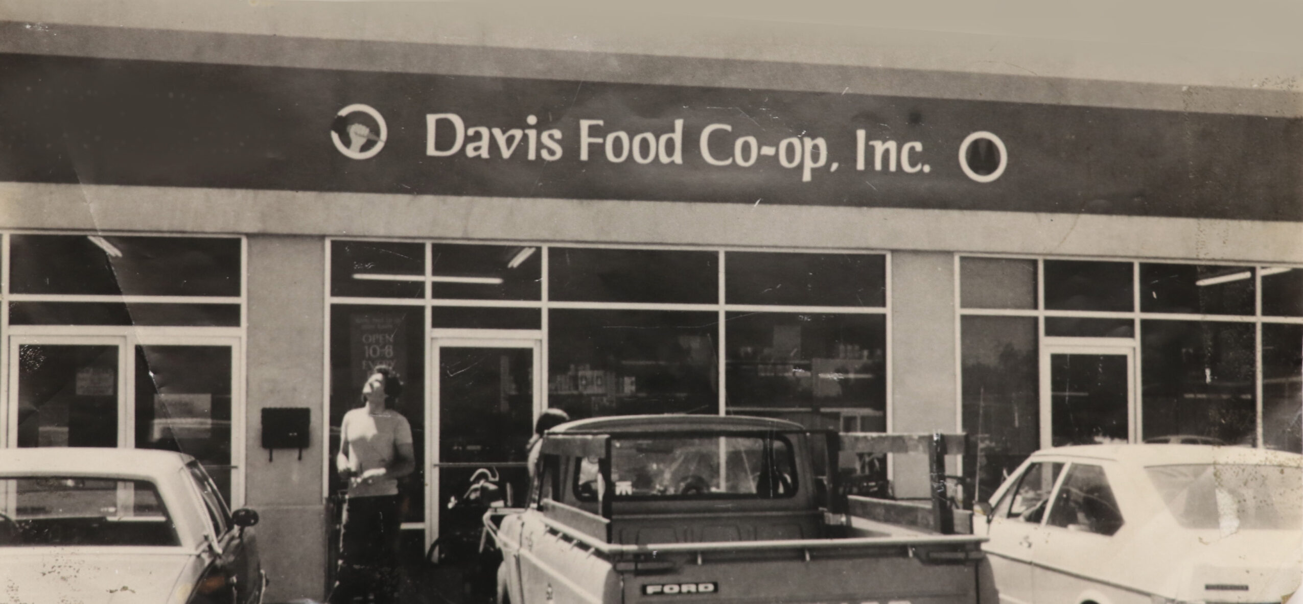 Storefront with sign reading 'Davis Food Co-op Inc.', three cars parked outside, and a person standing near the entrance.