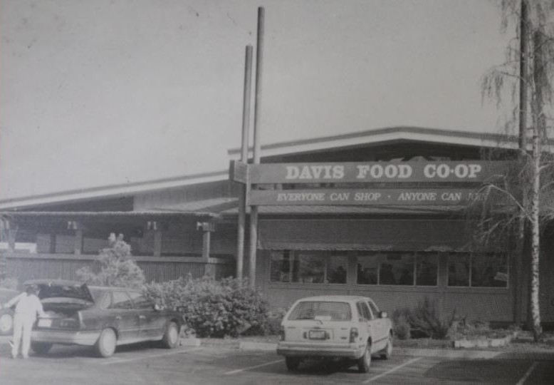 Storefront with a sign reading 'Davis Food Co-op' and parked cars in front.