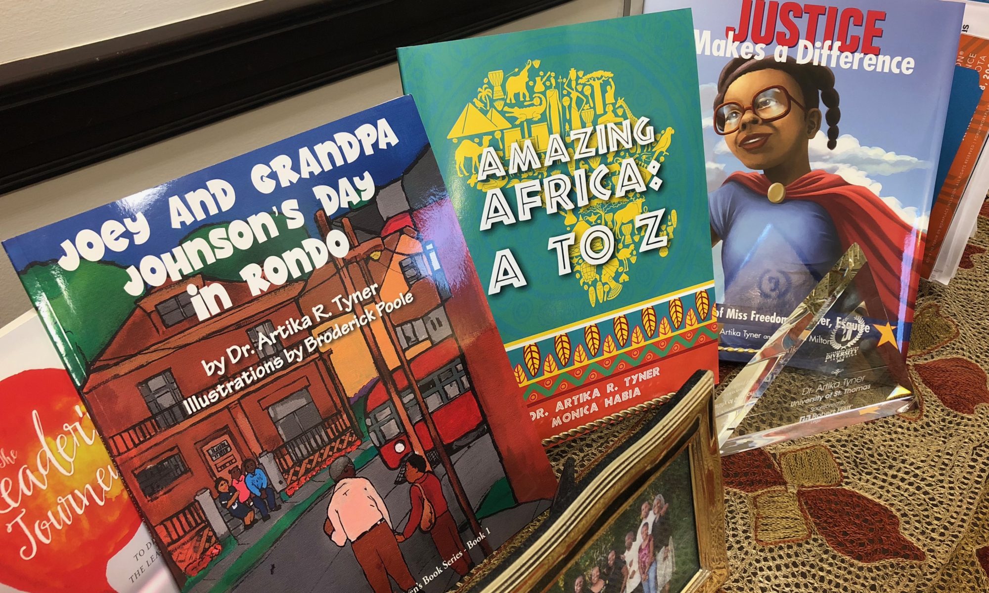 Collection of children's books displayed upright on a shelf, featuring colorful covers with titles about Africa, history, and superheroes.