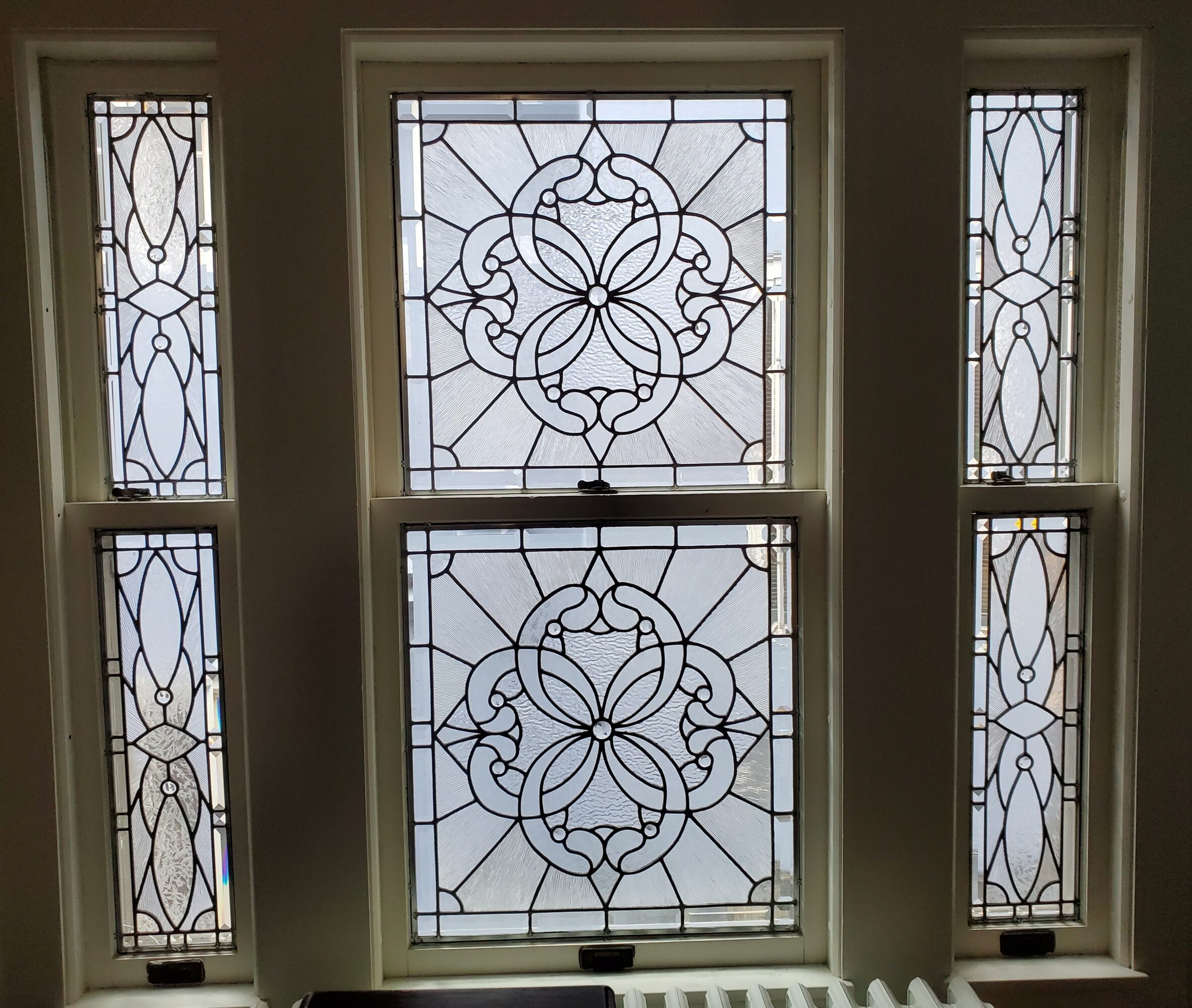 Four stained glass windows with intricate geometric patterns, two large central windows and two narrow side windows.
