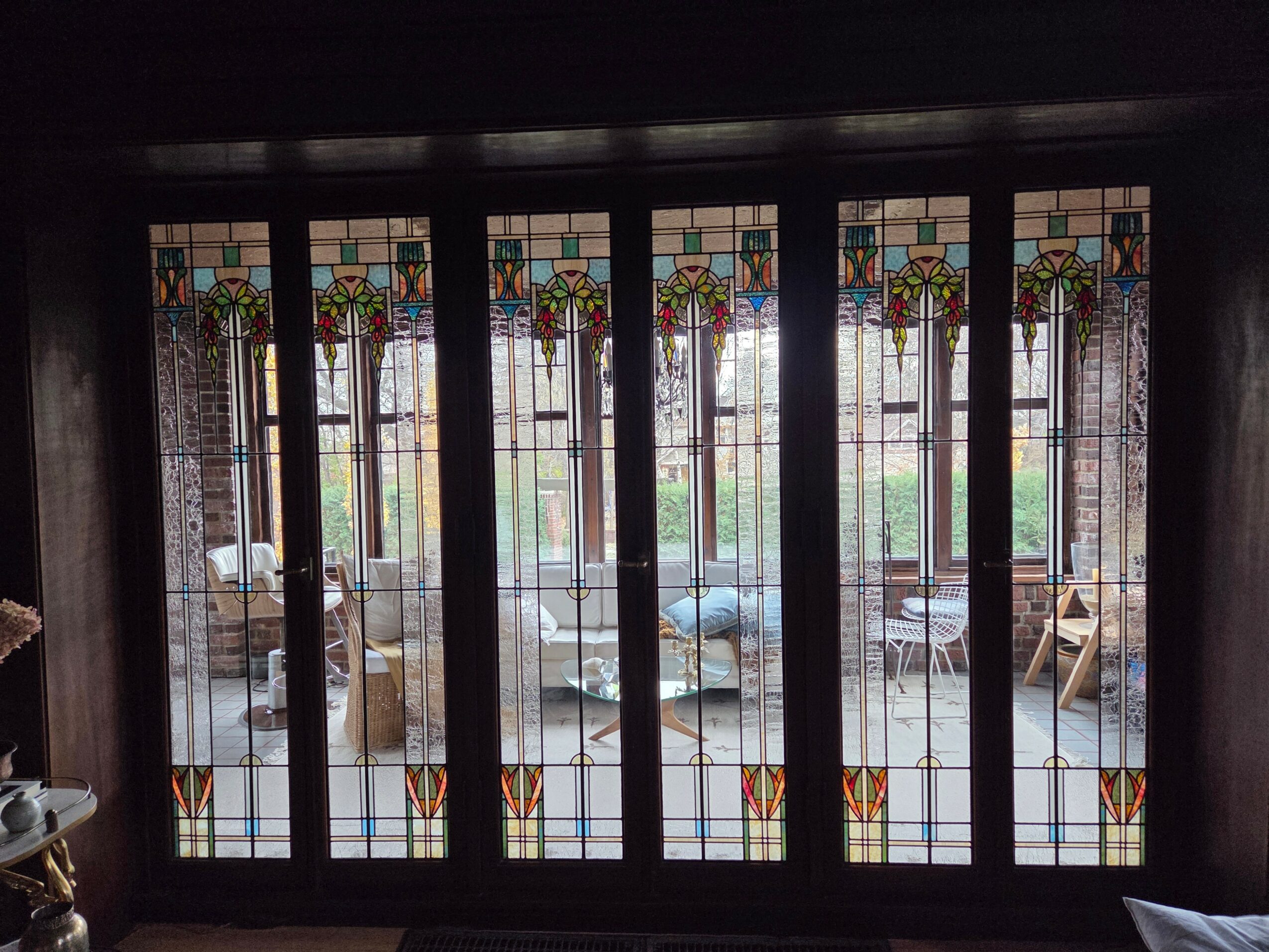 View through stained glass window showing outdoor patio with chairs and tables, and a person standing outside.
