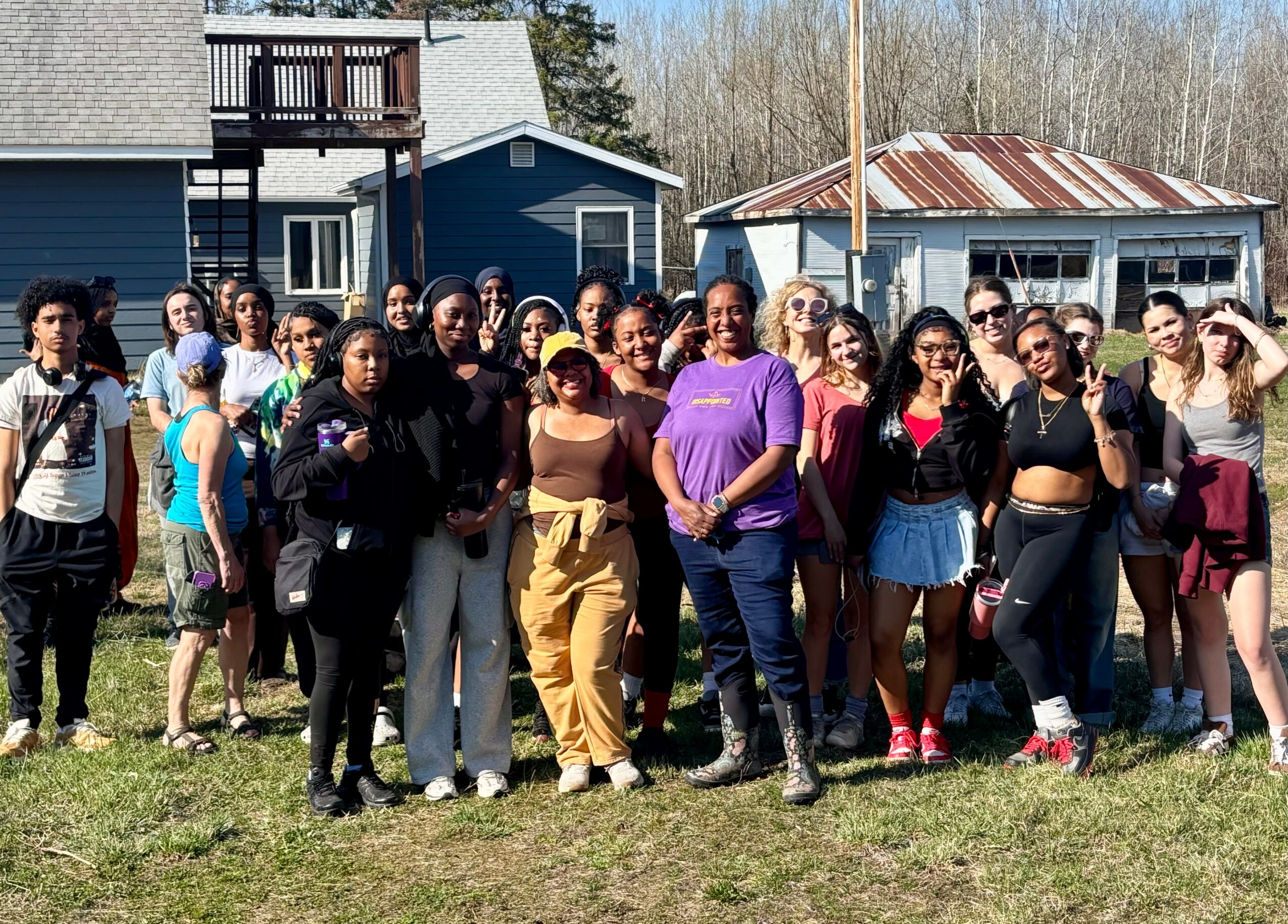 Group of people standing outdoors in front of houses, some smiling and posing for the photo.