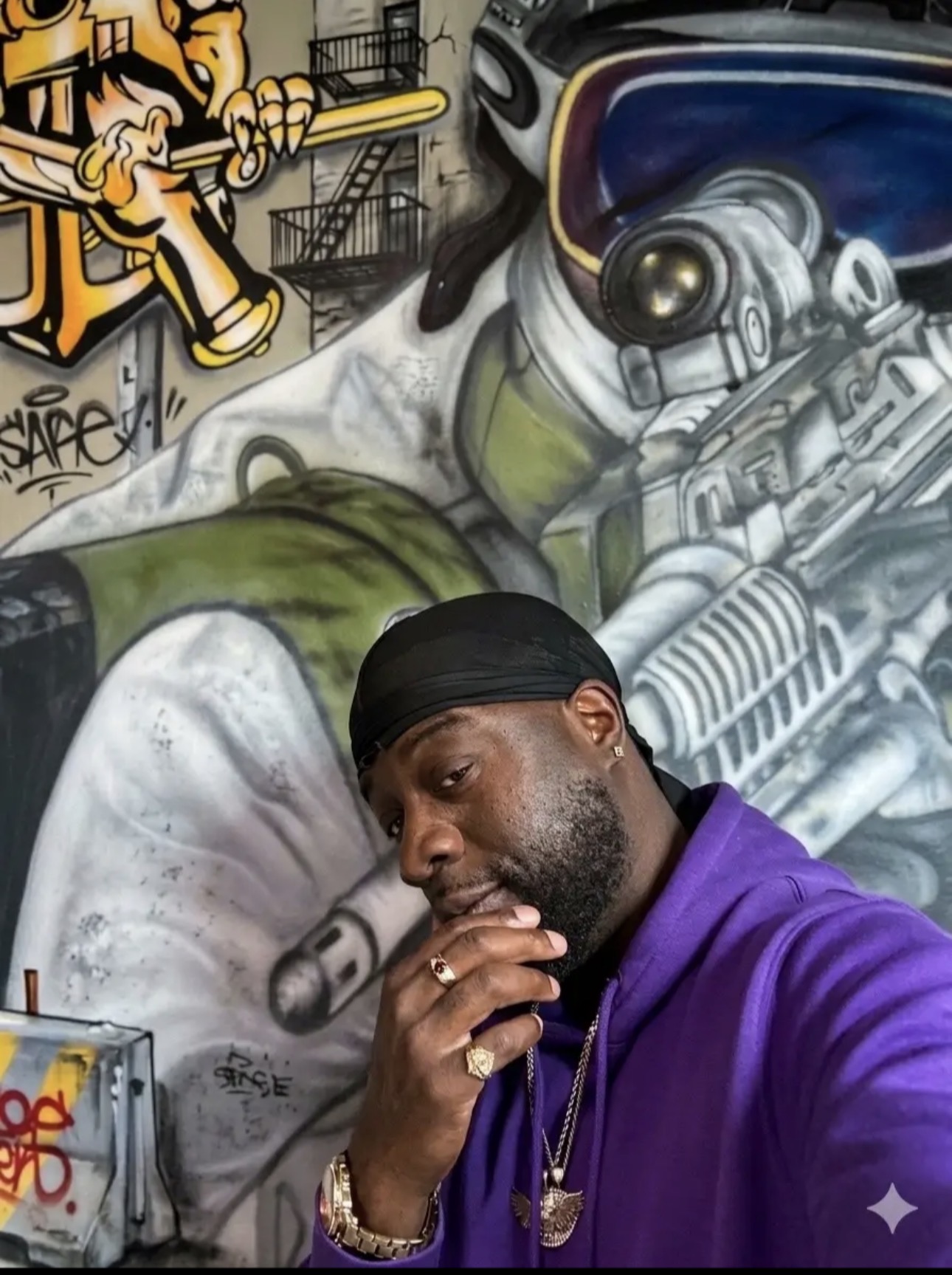 Man in purple hoodie with hand near face, graffiti mural background with a robot and cartoon characters