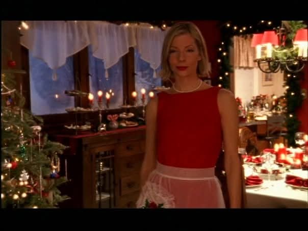 Woman in red dress standing in decorated room with Christmas lights and table setting.