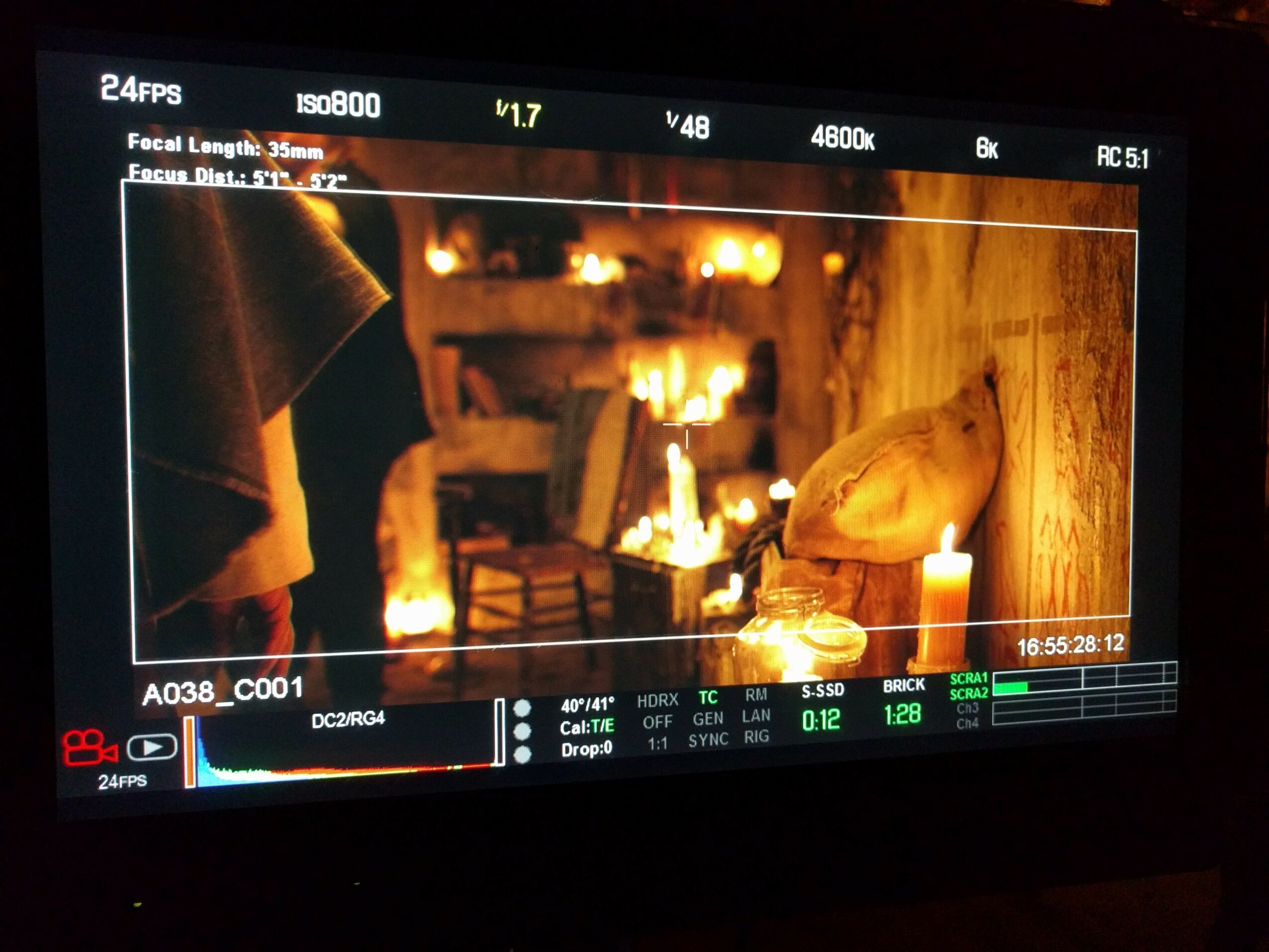 View through a camera monitor showing a cozy room with warm lighting, a person, and a table with a bag on it.