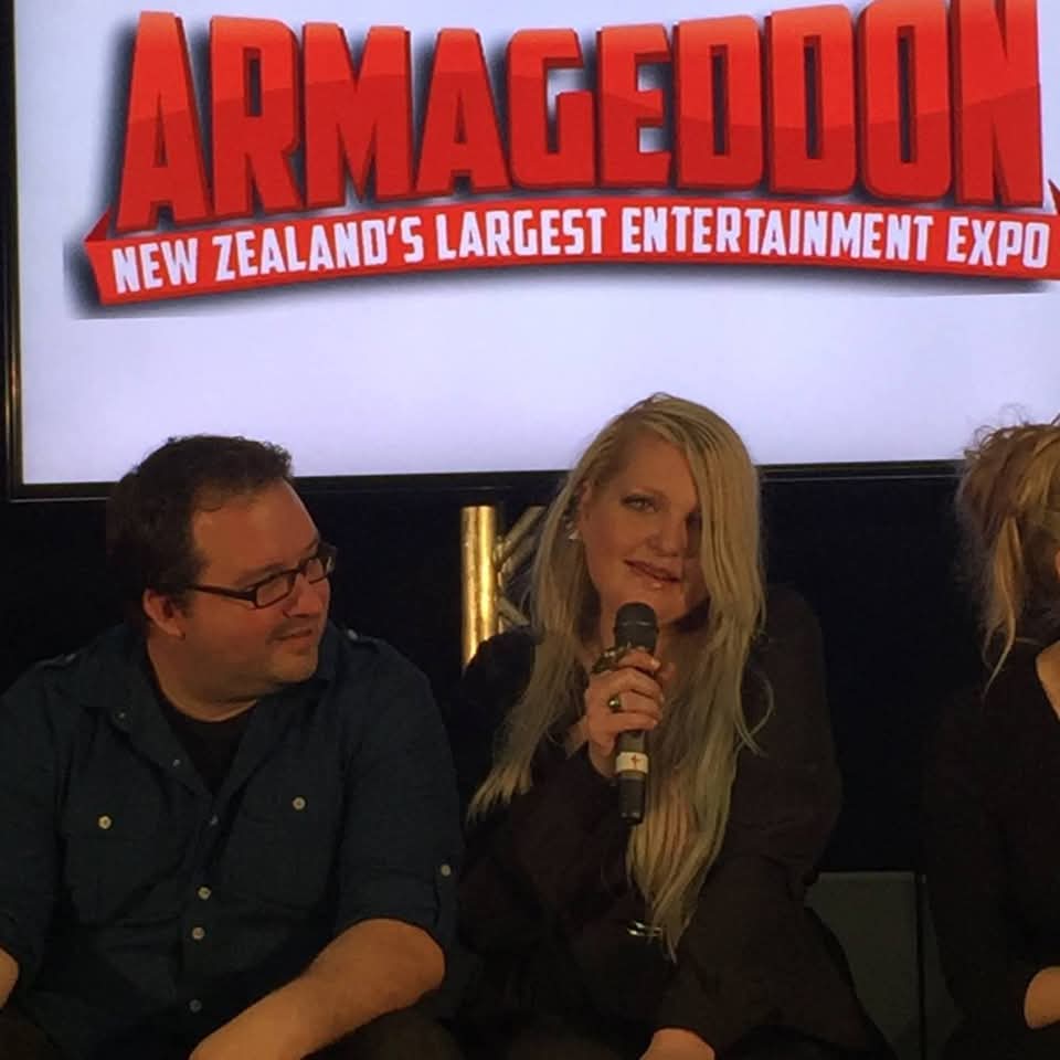 Three people sitting in front of a screen with the word 'ARMAGEDDON' and a subtitle about New Zealand's largest entertainment expo.