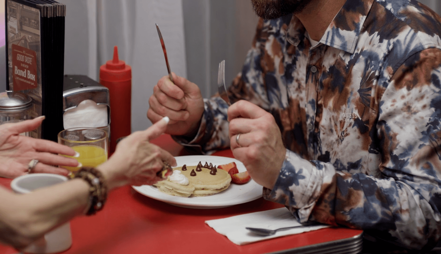 People sitting at a table sharing a plate of food, with condiments and utensils visible.