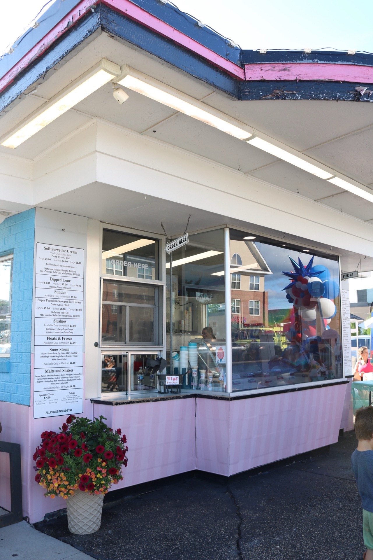 Ice cream stand with large window display, colorful decorations, and a person inside, outside on a sunny day.