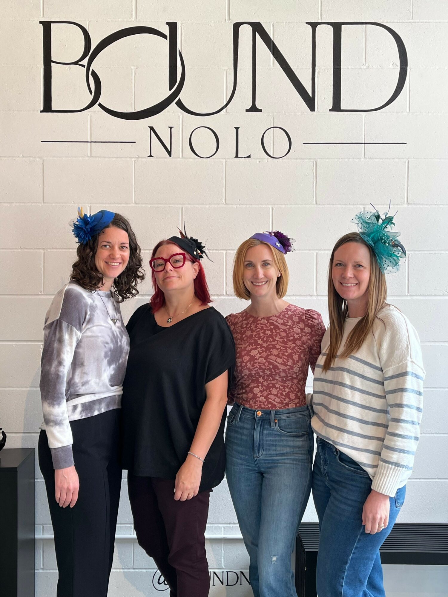 Four women standing against a tiled wall, smiling, with text reading 'BOUND ONO' on the left side.