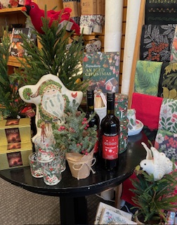 Table with Christmas decorations, including a Santa figure, wine bottles, a white rabbit figurine, and potted plants, in a store.