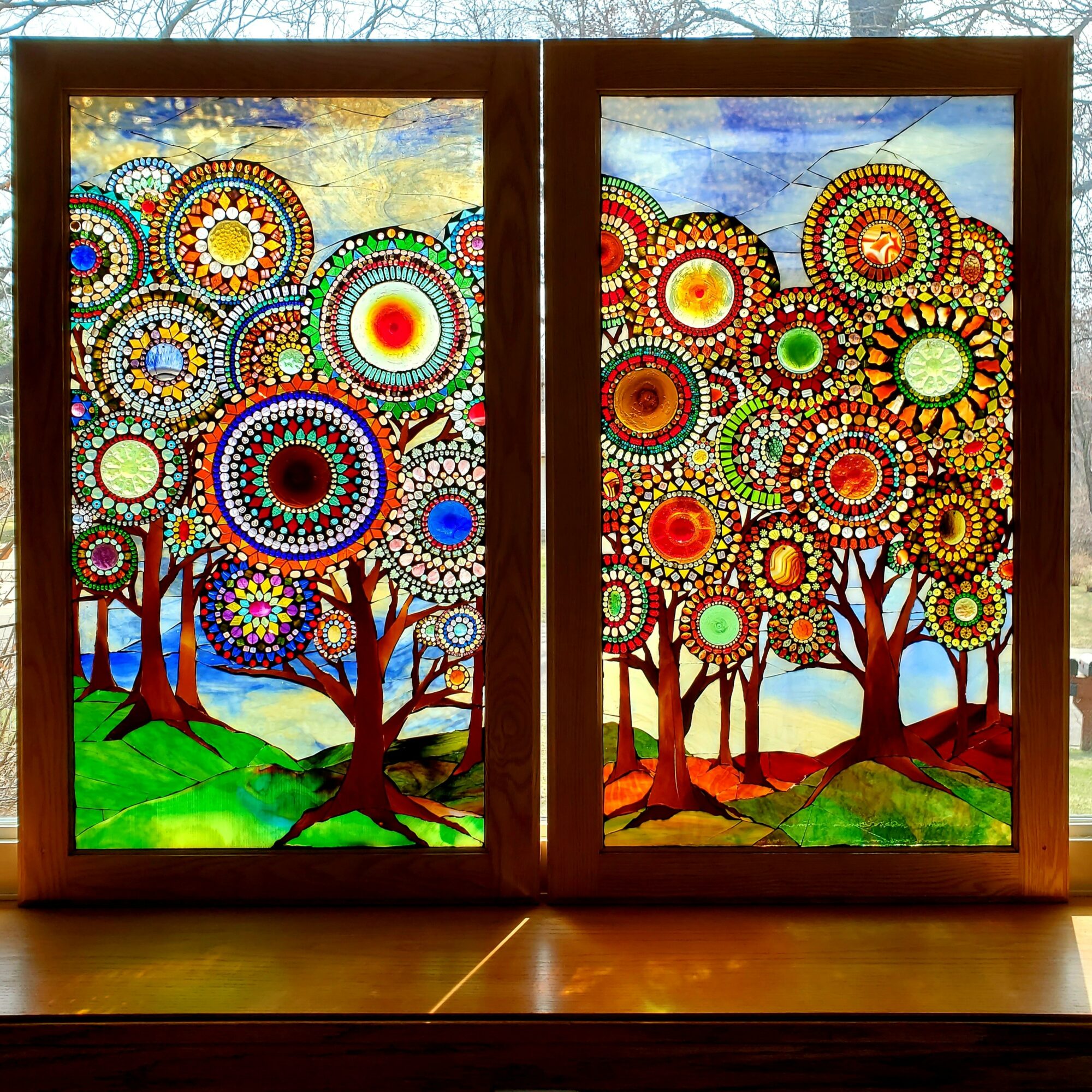 Two stained glass windows depict colorful, abstract trees with circular patterns, set against a sky and landscape background.