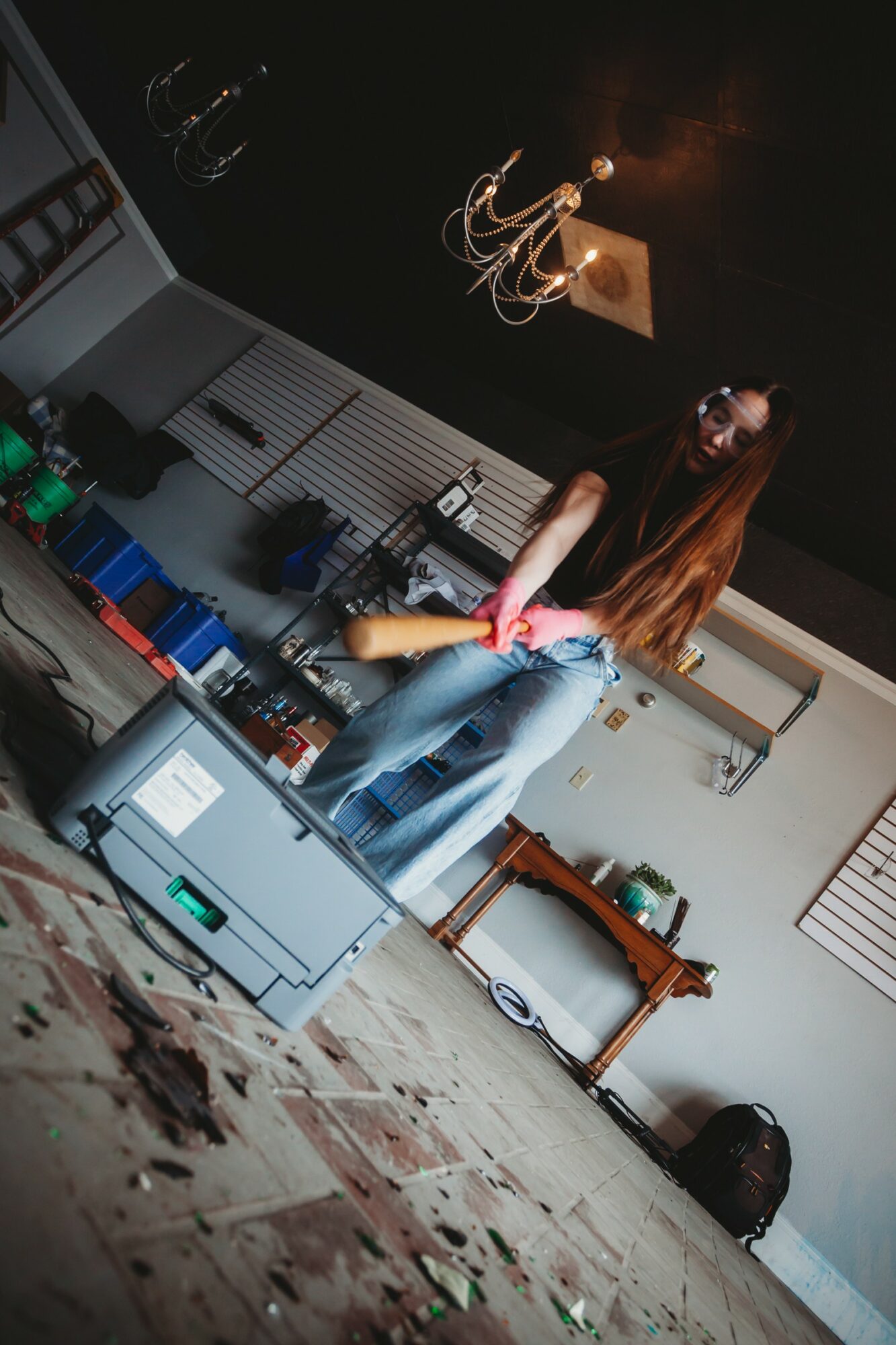 Person with long hair sitting on a stool in a room with kitchen cabinets, a table, and a ceiling light fixture.