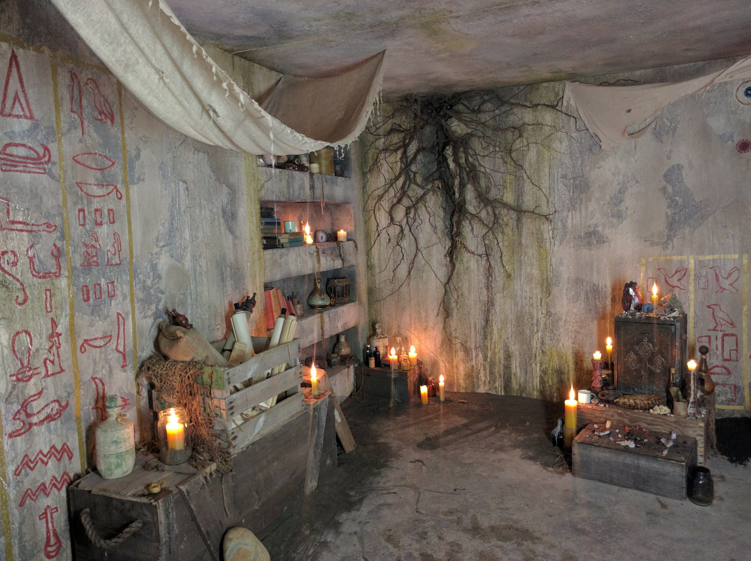 Interior of a cave with candles, ancient artifacts, and wall carvings, illuminated softly, with a rough ceiling and stone walls.